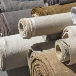 Close up assorted rolls of white, beige and brown flax linen fabric and canvas textile on retail market stall, high angle view