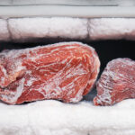 Big chunks of red beef lying on the freezer shelves with a big quantity of frozen ice and snow. This freezer hasn't been thawed in a long time.