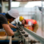 Technician or worker or engineer man look through rail of machine to his co-worker in the other side and they work in the factory.