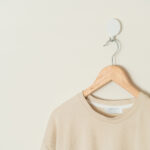 beige t-shirt hanging with wood hanger on wall