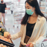 Young woman wearing protect face mask shopping in supermarket. asian woman wearing medical mask shopping in grocery store during coronavirus pandemic.  coronavirus crisis, covid19 outbreak.